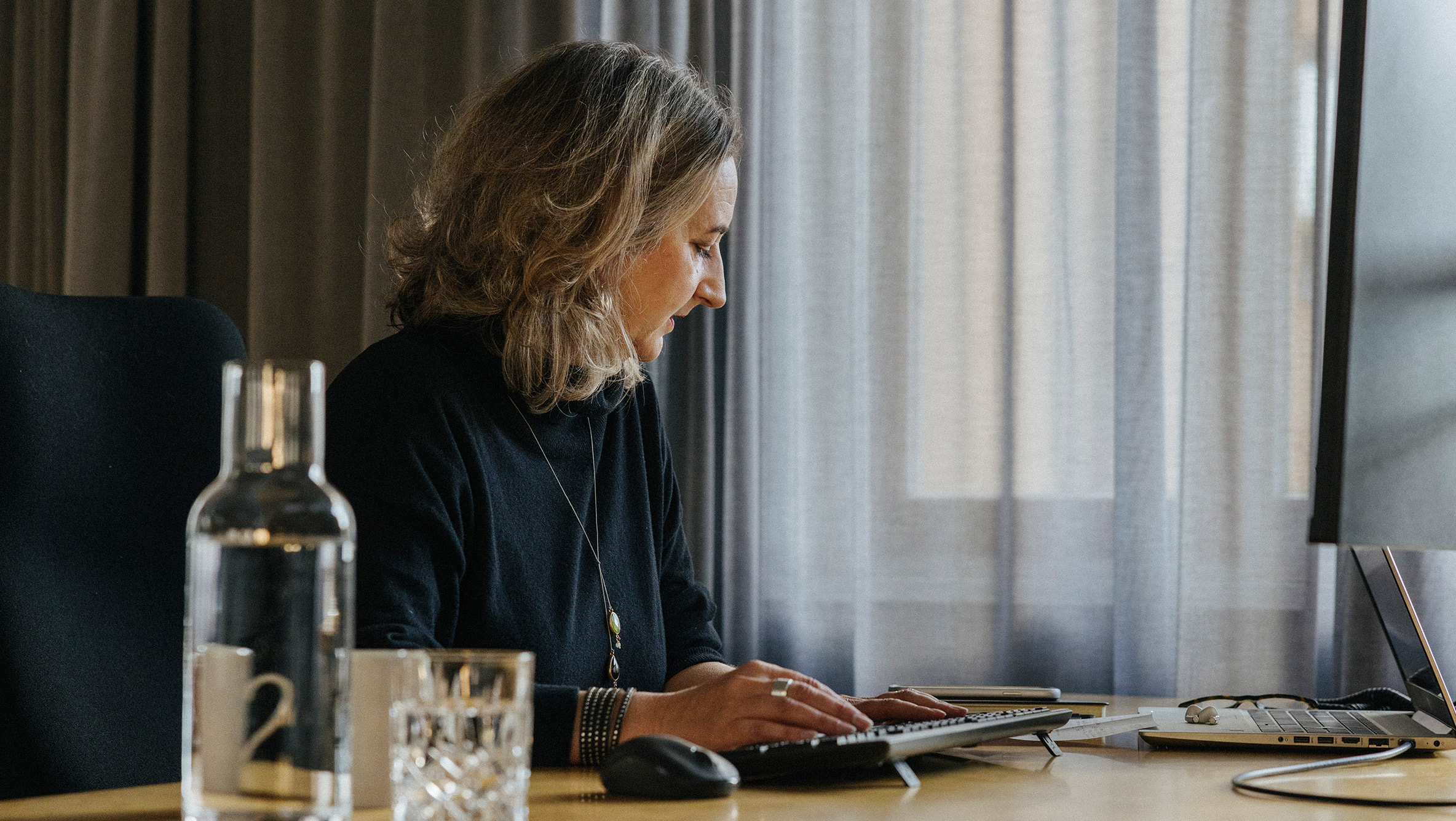 Seitliche Nahaufnahme von Partnerin Petra Stahl. Sie sitzt an ihrem Schreibtisch und blickt auf ein Dokument vor ihr, während sie auf der Tastatur tippt.